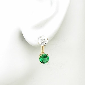 May include: Gold earrings with a single green gemstone and a single clear gemstone.