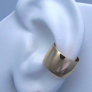 May include: A pair of gold earrings with a large, clear cubic zirconia stone on one earring and a gold cuff on the other.