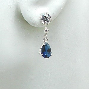 May include: Silver dangle earrings with a clear round stone at the top and a teardrop shaped blue stone at the bottom.
