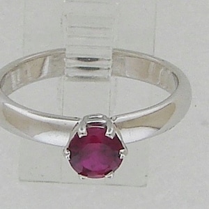 May include: A silver ring with a single round ruby gemstone set in a prong setting.