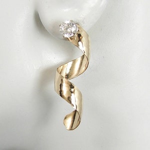 May include: Gold hammered metal earrings with a clear crystal stone at the top. The earrings are shaped like a spiral.