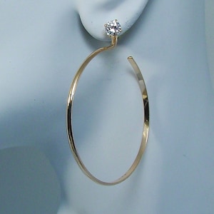 May include: Gold hoop earrings with a single clear crystal stone at the top of the hoop.