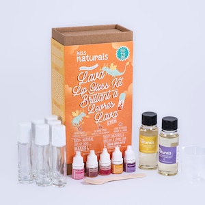 May include: A science kit for making lava lip gloss. The kit includes six clear glass bottles, four small bottles of colored liquid, a wooden spoon, a measuring cup, and two bottles of clear liquid labeled "naturals". The box is orange and features a cartoon dragon and the text "Lava Lip Gloss Kit Brillant a Levres Lava STEM".