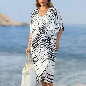 May include: A white and black tie-dye beach cover-up with a V-neck, short sleeves, and a tie at the waist. The cover-up is being worn by a person on a beach.
