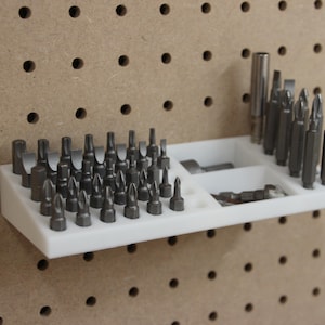 Könnte beinhalten: Ein weißer Bohrer-Organizer aus Kunststoff mit verschiedenen Metallbohrern. Der Organizer ist an einer Lochwand befestigt. Die Bohrer sind in verschiedenen Größen und Formen erhältlich und für verschiedene Aufgaben geeignet.
