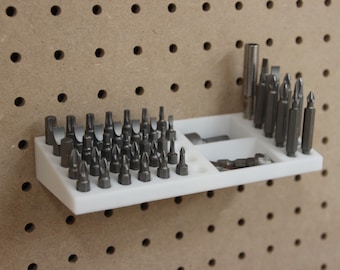 Pode incluir: Um organizador de brocas de plástico branco com várias brocas de metal. O organizador é montado em uma placa perfurada. As brocas são de diferentes tamanhos e formatos, adequadas para várias tarefas.