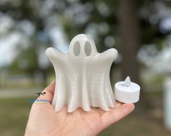 May include: White ghost-shaped candle holder with a small white LED tea light. The ghost has two eye holes and a wide, open mouth.