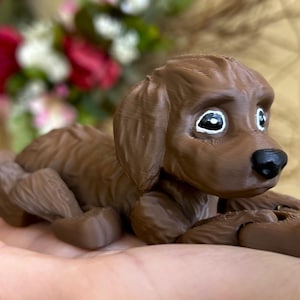 Peut inclure: Une figurine d'un chien couch&eacute; imprim&eacute;e en 3D de couleur marron. Le chien a des yeux peints en blanc et un nez noir.