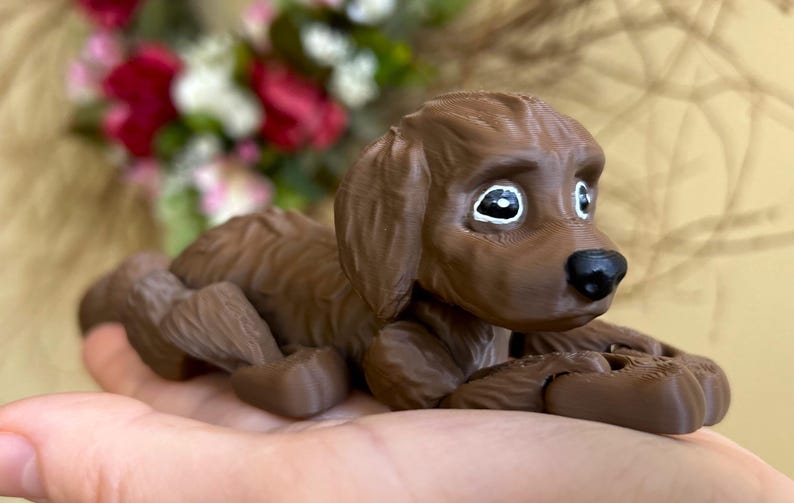 Peut inclure: Une figurine d'un chien couch&eacute; imprim&eacute;e en 3D de couleur marron. Le chien a des yeux peints en blanc et un nez noir.