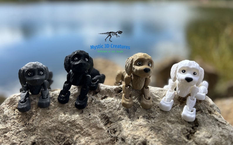 Peut inclure: Quatre figurines de chien articul&eacute;es, posables, imprim&eacute;es en 3D en noir, marron et blanc. Les figurines sont pos&eacute;es dans une position assise ludique. Le texte "Mystic 3D Creatures" est visible au-dessus des figurines.