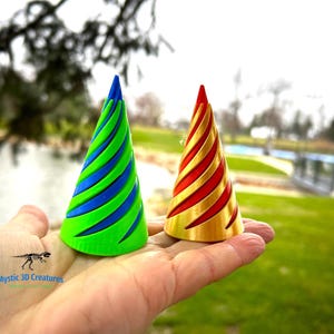 May include: Two small, cone-shaped party hats. One is green with blue stripes and the other is gold with red stripes.