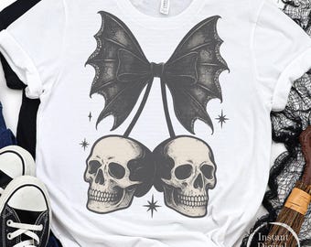 May include: White t-shirt featuring a black bat wing bow design with two skulls hanging below. The design includes star accents. The shirt is part of a Halloween or gothic-themed collection.