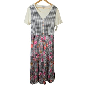 May include: A vintage-style dress with a cream-colored top and a plaid vest-like overlay. The dress features a floral print skirt with pink and red roses. The dress is hanging on a wooden hanger.