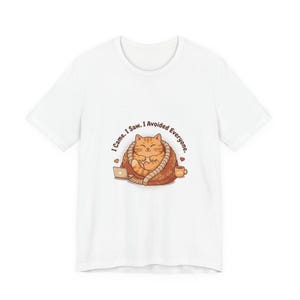Puede incluir: Camiseta blanca con un gato de dibujos animados envuelto en una manta, con un portátil y una taza de café. El gato es naranja y blanco, con el texto: "I came. I saw. I avoided everyone."