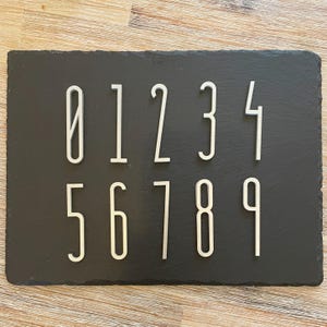 Könnte beinhalten: Eine schwarze Schieferplatte mit weißen Zahlen von 0 bis 9 in zwei Reihen angeordnet.