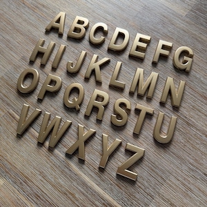May include: A complete set of twenty-six uppercase letters from A to Z, crafted in a metallic gold finish with a three-dimensional block font style. Each individual letter features clean, sharp edges and a smooth surface, arranged in rows.