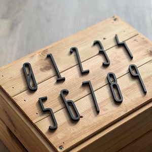 以下が含まれることがあります： 木製の表面に配置された、0から9までの黒いプラスチック製の数字。数字はモダンなフォントスタイルです。