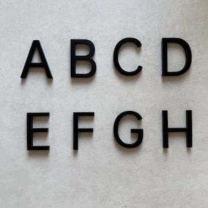 May include: Eight black uppercase letters, A to H, are displayed on a light grey surface. The letters are evenly spaced and appear to be made of a solid material. The font is a simple, sans-serif style. The letters are in a row.