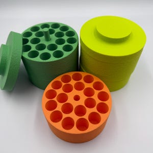 Puede incluir: Una colección de soportes cilíndricos coloridos con múltiples aberturas circulares. Los soportes son en tonos verdes, naranjas y amarillos. Un soporte verde tiene una tapa. Los soportes están diseñados para organizar objetos pequeños.