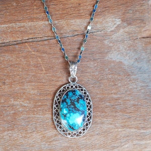 May include: A silver chain necklace with a pendant featuring a blue and black oval stone set in a silver filigree frame.