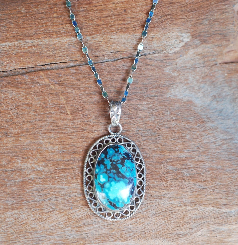 May include: A silver chain necklace with a pendant featuring a blue and black oval stone set in a silver filigree frame.