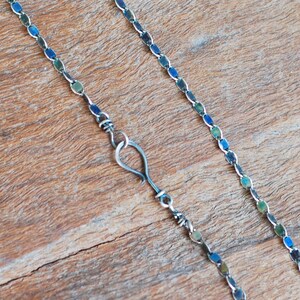 May include: A silver chain necklace with a hook clasp. The chain is made of small, oval-shaped links that have a blue and green iridescent finish.
