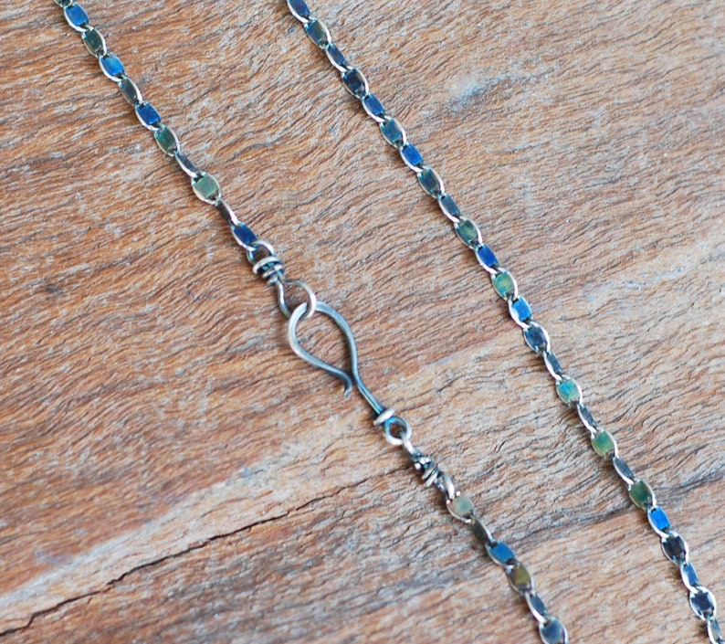 May include: A silver chain necklace with a hook clasp. The chain is made of small, oval-shaped links that have a blue and green iridescent finish.