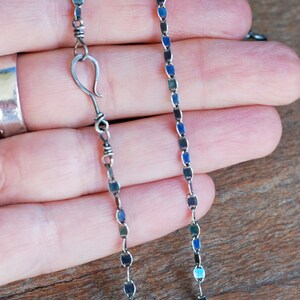 May include: A silver chain necklace with a lobster clasp closure. The chain is made of small, flat, oval-shaped links.