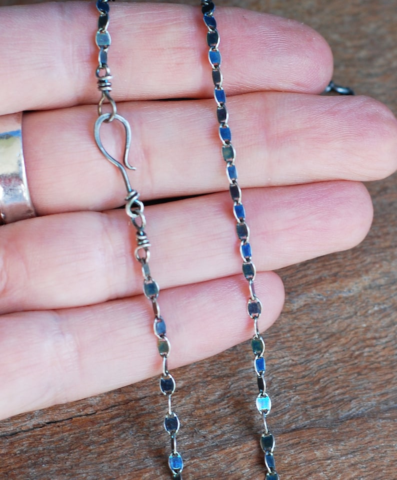 May include: A silver chain necklace with a lobster clasp closure. The chain is made of small, flat, oval-shaped links.