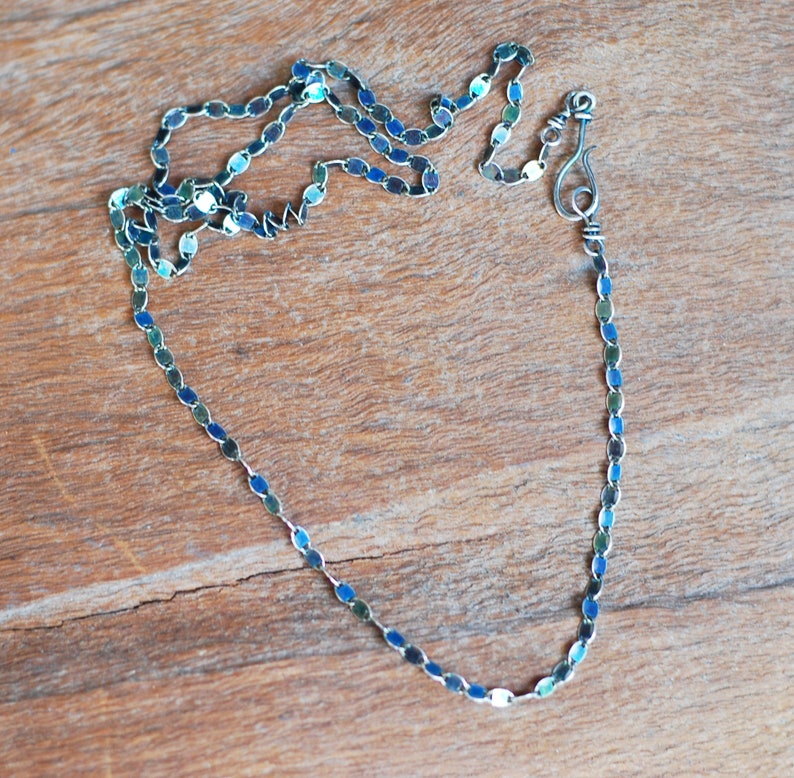 May include: A silver chain necklace with a blue and green iridescent finish. The chain is made of small oval links and has a simple hook clasp.