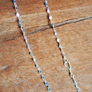 May include: A silver chain necklace with a delicate, oval-shaped link design. The chain is shown on a wooden surface.