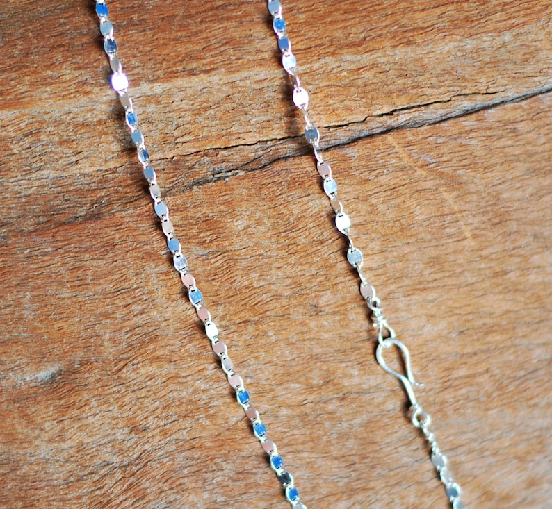May include: A silver chain necklace with a delicate, oval-shaped link design. The chain is shown on a wooden surface.