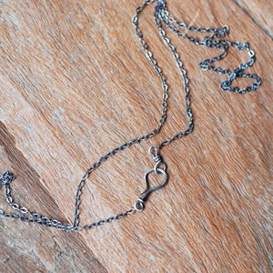 May include: A silver chain necklace with a heart-shaped pendant. The necklace is lying on a wooden surface.