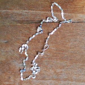 May include: A silver chain necklace with a delicate, flat, oval link design. The chain is on a wooden surface.
