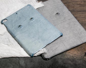 May include: Two tablet cases, one light blue and one gray, with painted eyes on the front. The cases are made of a textured material and have a slightly worn look.