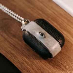 Könnte beinhalten: Ein schwarzes Lederetui mit einer silbernen Kette und einem silbernen Ösendetail. Das Etui hat einen weißen Lederbesatz und ist für die Aufbewahrung eines kleinen elektronischen Geräts konzipiert.