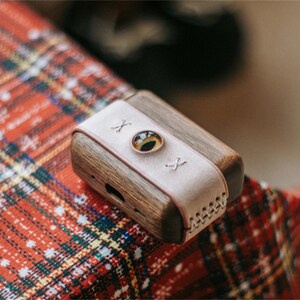May include: A small, wooden box with a leather strap and a round, clear window. The box is on a red and white checked surface.