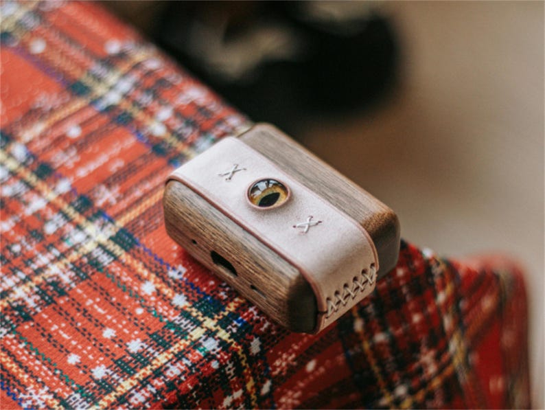 May include: A small, wooden box with a leather strap and a round, clear window. The box is on a red and white checked surface.