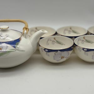 May include: A white ceramic tea set with a teapot and six matching teacups. The teapot has a bamboo handle and a blue band with floral designs. The teacups also have a blue band and floral designs. The set is on a white surface.