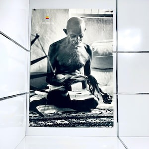 Könnte beinhalten: Schwarz-Weiß-Poster mit einer sitzenden Figur mit Brille, die liest. Das Apple-Logo und die Worte "Think different" befinden sich in der oberen linken Ecke. Das Poster wird in einem weiß gefliesten Raum angezeigt.