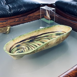 Può includere: Un piatto da portata in ceramica con un design a spirale verde, marrone e bianco. Il piatto è di forma ovale e ha un bordo leggermente rialzato.