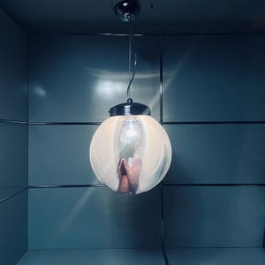 May include: A modern, spherical pendant light with a chrome finish and a frosted glass shade. The light fixture hangs from a single wire and illuminates a room with a warm glow. The interior of the shade has a pinkish hue.