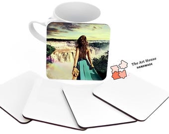 May include: A white ceramic mug with a colorful image of a woman standing in front of a waterfall. The mug is surrounded by four blank white coasters with black edges. The text "The Art House HANDMADE" is visible in the image.