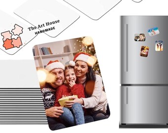 May include: A set of square photo magnets featuring a family photo of a man, woman, and child in front of a Christmas tree. The magnets are on a silver refrigerator. The magnets are printed with "The Art House Handmade" on the back.
