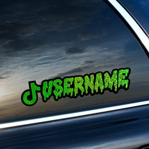 May include: A green glitter sticker with the word "USERNAME" in a dripping font, outlined in black. The sticker is affixed to a car window, with a cloudy sky visible in the background.