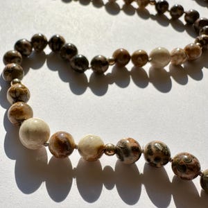 May include: A long necklace made of brown, white, and gray agate beads. The beads are round and have a natural, organic look.