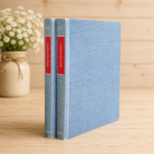 Può includere: Due libri con copertina rigida abbinati e rivestimento in tessuto azzurro. Ogni dorso presenta un'etichetta rettangolare rossa con il testo bianco "Loyalists in East Florida" e un piccolo numero romano in basso, indicante il volume uno e due.