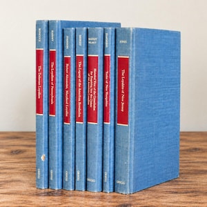 May include: A collection of seven blue hardback books arranged in a row. Each spine displays a red rectangular label with white lettering, featuring titles such as The Delaware Loyalists, The Loyalists of Pennsylvania, and The Loyalists of New Jersey, with Gregg at the base.
