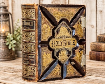 Op de afbeelding: Een antieke Heilige Bijbel met een donkerbruine leren kaft voorzien van gedetailleerde goudkleurige illustraties en belettering. De rug toont de tekst Holy Bible en New Testament, met metalen sluitingen aan de zijkant en een afgeschuind ontwerp.