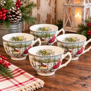 May include: Four white ceramic tea cups featuring a detailed winter landscape illustration with red barns, bare trees, and snow-covered ground. Each cup has a handle and a decorative border pattern along the rim, showcasing a consistent seasonal scene.
